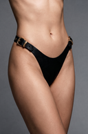 woman wearing black leather panties with gold-tone buckle details, photographed against a neutral gray studio background.